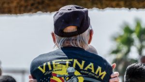 A Vietnam Veteran stands with his back to the camera, wearing a jacket that says, "All gave some, some gave all."