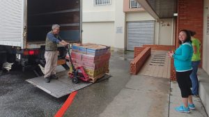 Sakumoto Toshiro, tracker-trailer driver for the Okinawa Distribution Center, unloads boxes of Girl Scout cookies for expectant Girl Scouts volunteers.