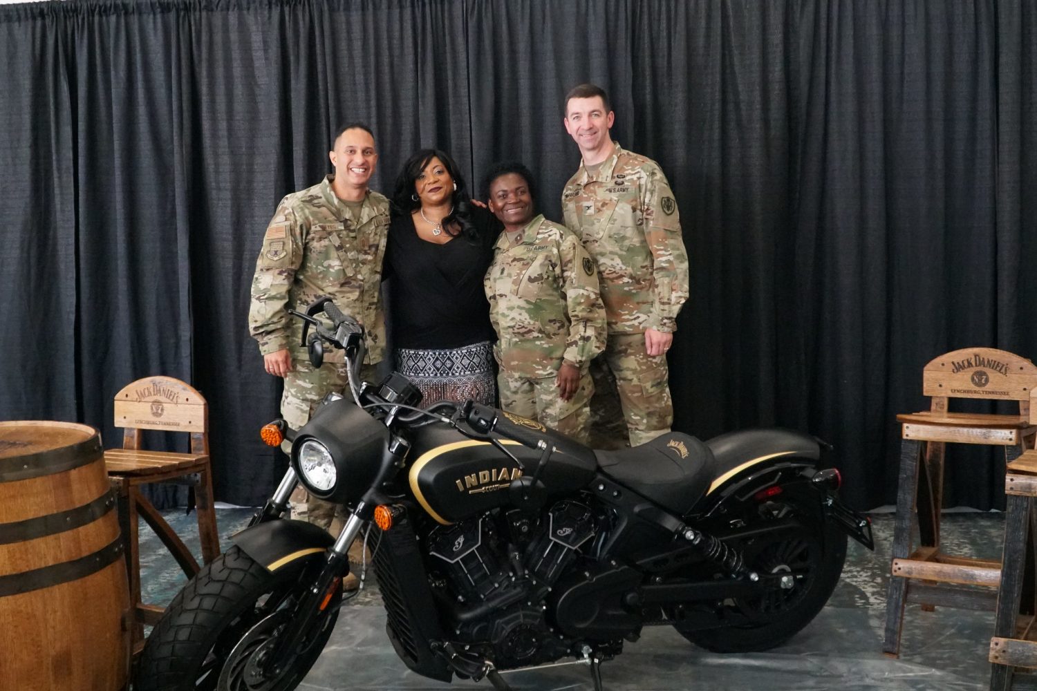 Three Soldiers in uniform stand with an Army veteran behind an Indian motorcycle