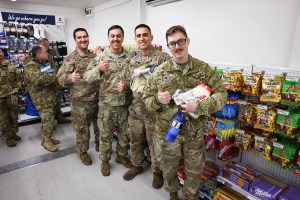 Soldiers holding snacks and beverages while giving a thumbs up to the camera